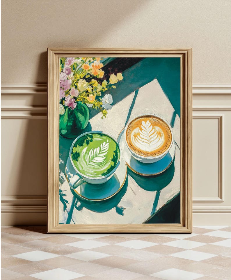 May include: A framed painting of two cups of coffee with latte art. One cup is green and the other is brown. The cups are on a white table with a vase of flowers in the background.