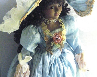 Elegante muñeca de porcelana negra: vestido de alta costura de la Edad Dorada, sombrero adornado.