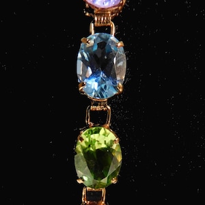 Peut inclure: Un bracelet en or avec quatre pierres précieuses rondes. Les pierres précieuses sont violettes, bleues, vertes et rouges.