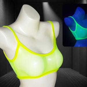May include: A neon yellow sports bra with thin straps and a matching trim is displayed on a mannequin. The bra is shown in a dark room with a glowing effect, and a smaller image shows the bra glowing under a black light.