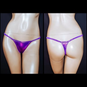 May include: A pair of metallic purple thong underwear. The front and back views are displayed, showcasing the shiny fabric and delicate string design. The underwear is displayed on a mannequin.