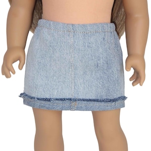 May include: A light blue denim mini skirt with a faded wash, featuring a straight cut, an elasticized waistband, and a frayed, raw-edge hemline. The skirt is constructed from a textured cotton fabric with visible stitching along the center front.