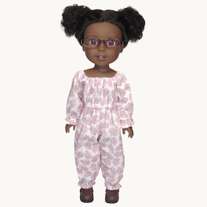 May include: A doll with dark skin, wearing glasses and a pink and white patterned jumpsuit. The doll has black curly hair styled in two buns and brown shoes. The jumpsuit has a square neckline and long sleeves with ruffled cuffs.