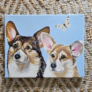 May include: Painting of two corgi dogs with a butterfly above them. The corgis are painted in a realistic style with brown, black, and white fur. The background is a light blue.