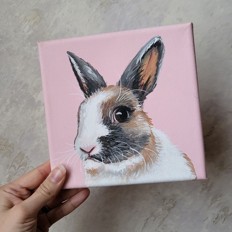 May include: A painting of a brown and white rabbit with black markings on a pink background.