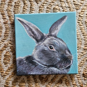 May include: A painting of a gray rabbit with brown eyes on a light blue background.