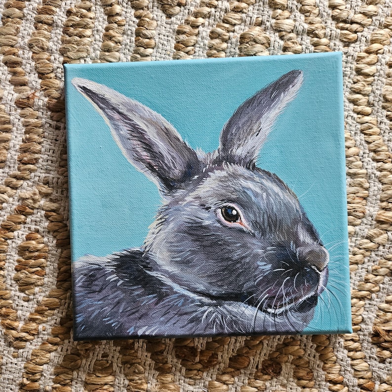 May include: A painting of a gray rabbit with brown eyes on a light blue background.