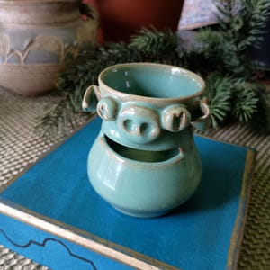 May include: A set of three ceramic mugs with a speckled, matte finish. The mugs are in shades of cream, light gray, and dark gray. Each mug has a simple, minimalist design and a rounded handle. The mugs are stacked on top of each other.