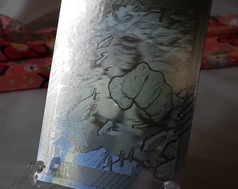 May include: A silver foil trading card with a black and white illustration of a fist breaking through a wall. The fist is green and the wall is gray.