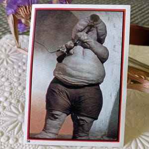 May include: A vintage trading card featuring a black and white image of a person with a distorted body. The person is wearing dark shorts and boots. The card has a red border and the number 58 in the bottom left corner.