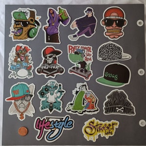 May include: A collection of colorful stickers with urban and hip-hop themes. The stickers feature cartoon characters, skulls, and text like "Swag" and "Lifestyle." The designs include a bear with headphones, a dinosaur DJ, and a bulldog with a gold chain.