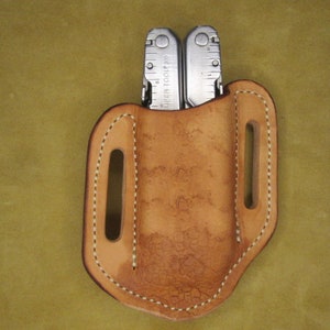 May include: A tan leather sheath with a stitched edge for a multi-tool. The sheath has two belt loops.