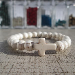 Peut inclure: Bracelet en perles blanches avec un pendentif en forme de croix blanche. Le bracelet est composé de petites perles rondes et présente un design simple et élégant.
