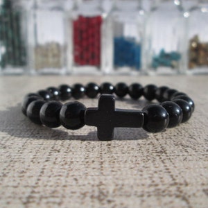 Peut inclure: Un bracelet en perles noires avec un pendentif en forme de croix noire. Le bracelet est composé de perles rondes et la croix est un design simple.