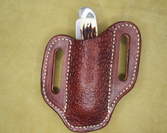 May include: A brown leather pocket knife sheath with white stitching. The sheath has a belt loop and a flap that secures with a snap.