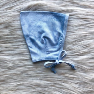 Può includere: Un berretto per neonato di colore azzurro tie-dye con un fiocco bianco e un bordo bianco.