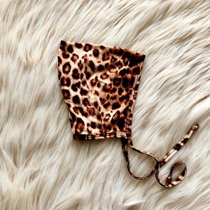 Puede incluir: Un gorro de bebé de color marrón y beige con estampado de leopardo y cierre de lazo.