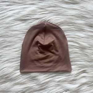 May include: A brown beanie made of soft, stretchy fabric. The beanie is plain and has no embellishments.