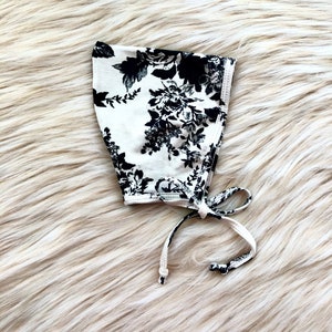 May include: A white bonnet with a black floral print and white ties.