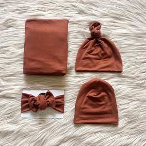 May include: A set of three brown baby accessories: a knotted beanie, a plain beanie, and a headband with a bow. The headband has the text "Stella Jane & Co. Headband" printed on a white card.