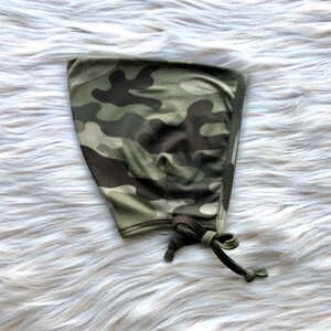 Puede incluir: Un gorro de tela de camuflaje verde y marrón con un cordón de ajuste.