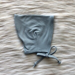 May include: A light blue baby bonnet with a tie closure. The bonnet is made of a soft, stretchy fabric.
