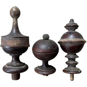 May include: Three antique wooden finials in various shapes and sizes. The finials are dark brown and have a worn, aged appearance.
