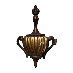 May include: A gold and brown decorative finial with a fluted design and two handles. The finial is shaped like a vase or urn.
