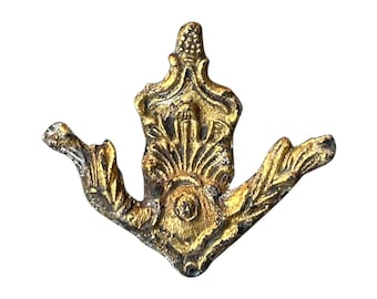 May include: Ornate, antique-style gold-colored furniture applique. The decorative piece features a central, vertical design with a detailed, textured surface and two curved, wing-like extensions. The metal has a distressed finish.