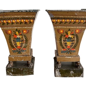May include: A pair of antique, hand-painted metal planters with a brown base and floral designs in shades of red, yellow, blue, and green. The planters have a flared, trumpet-shaped design and stand on a square base with four feet.