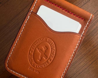 May include: A tan leather cardholder with white stitching and a red accent stitch. The cardholder features an embossed logo that reads "Bethpage State Park Black Course EST. 1936". A white card is partially visible in the front pocket.