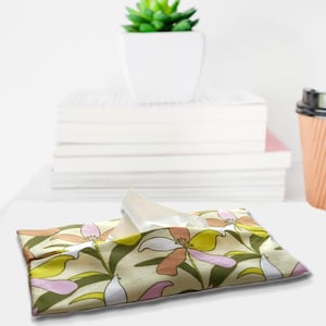 May include: A rectangular fabric tissue holder featuring a floral pattern with stylized lily-like flowers in shades of olive green, soft pink, and white on a light cream background, with a single white tissue protruding from the center opening.