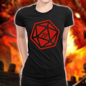 May include: Black t-shirt featuring a red 20-sided die graphic. The die has a black outline and the number 20 is printed in white inside the die.