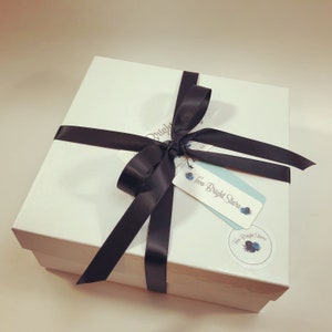May include: A white gift box tied with a black satin ribbon. The box has a tag that reads "Two Bright Stars" with a floral design. A matching sticker is also on the box.