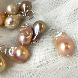 May include: A collection of irregularly shaped, iridescent pearls with silver-tone findings. The pearls display a range of colors, including cream, pink, and lavender, and are set against a white, textured background. These pearls are ideal for jewelry making.