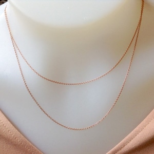 Peut inclure: Un collier délicat en or rose avec deux chaînes fines. Le collier est présenté sur un mannequin blanc, mettant en valeur son design superposé. Les chaînes sont symétriques et tombent avec grâce.