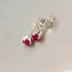 May include: A pair of silver stud earrings featuring vibrant red gemstones. The earrings have a classic design, with the red stones set in a four-prong setting. The posts and backs are also silver.
