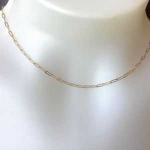 May include: A delicate gold-coloured paperclip chain necklace. The necklace is displayed on a white mannequin bust. The chain is made of small, rectangular links.