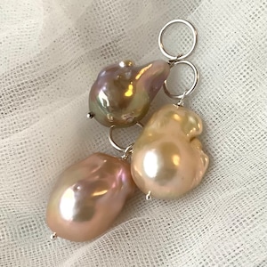 May include: Three baroque pearl pendants with silver-tone findings. The pearls have a lustrous sheen, displaying shades of pink, cream, and iridescent hues. The irregular shapes of the pearls add to their unique appeal. The pendants are likely for earrings or a necklace.