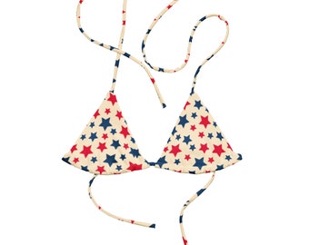 May include: A cream-colored bikini top with red and blue stars. The top has adjustable straps and ties at the back.