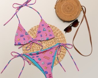 Könnte beinhalten: Pinkfarbener und blauer Bikini mit geometrischem Muster, dazu eine passende Strohtasche und Sonnenbrille.