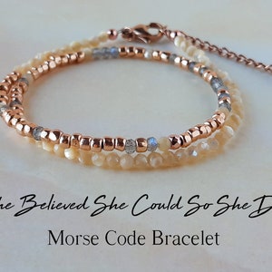 May include: A double-strand bracelet with a rose gold chain and beads, white and gray beads, and a clasp. The bracelet has the text "She Believed She Could So She Did" and "Morse Code Bracelet" written below it.