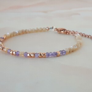 K&ouml;nnte beinhalten: Ein zartes Armband mit einer Mischung aus hellgelben und violetten Perlen, akzentuiert mit goldfarbenen Zwischenst&uuml;cken. Das Armband hat einen Karabinerverschluss und einen kleinen Anh&auml;nger.