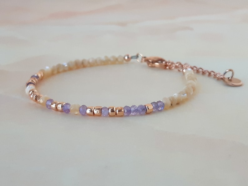 K&ouml;nnte beinhalten: Ein zartes Armband mit einer Mischung aus hellgelben und violetten Perlen, akzentuiert mit goldfarbenen Zwischenst&uuml;cken. Das Armband hat einen Karabinerverschluss und einen kleinen Anh&auml;nger.