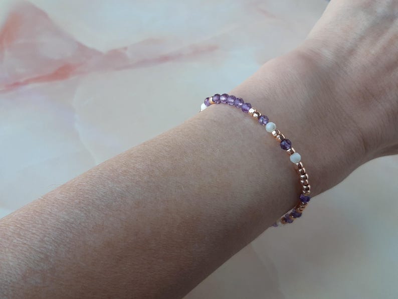 Op de afbeelding: Een delicate armband met afwisselende paarse en witte kralen op een ros&eacute;gouden ketting.