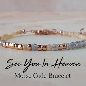 Könnte beinhalten: Ein zartes Armband aus kleinen Perlen in Beige-, Grau- und Roségoldtönen. Das Armband trägt die Botschaft "See You In Heaven" in Morsecode.