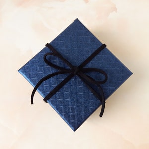 May include: A dark blue gift box with a black velvet ribbon tied in a bow.