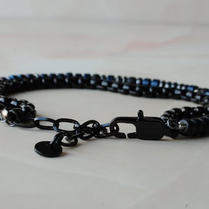 May include: A black beaded bracelet with a black metal clasp and chain. The beads are a mix of black and blue.