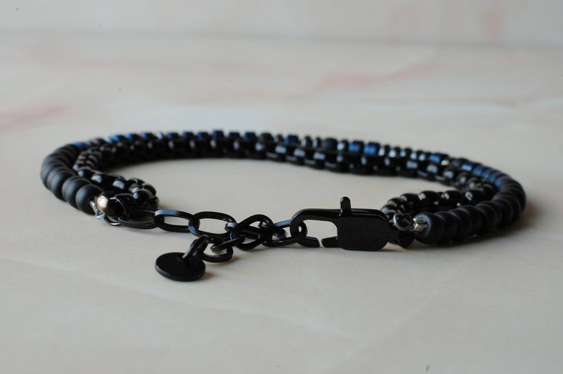 May include: A black beaded bracelet with a black metal clasp and chain. The beads are a mix of black and blue.