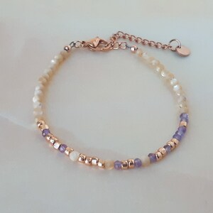 K&ouml;nnte beinhalten: Ein zartes Armband mit einer Mischung aus wei&szlig;en und gelben Perlen, akzentuiert mit kleinen lila Perlen und einem ros&eacute;goldenen Verschluss.